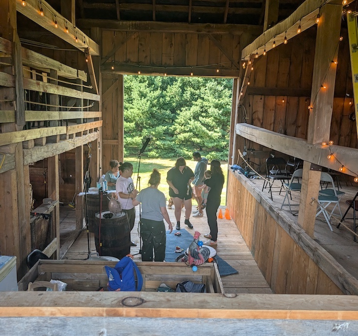 A bunch of people milling around the floor of a wooden barn with a big mic set up A bunch of people milling around the floor of a wooden barn with a big mic set up