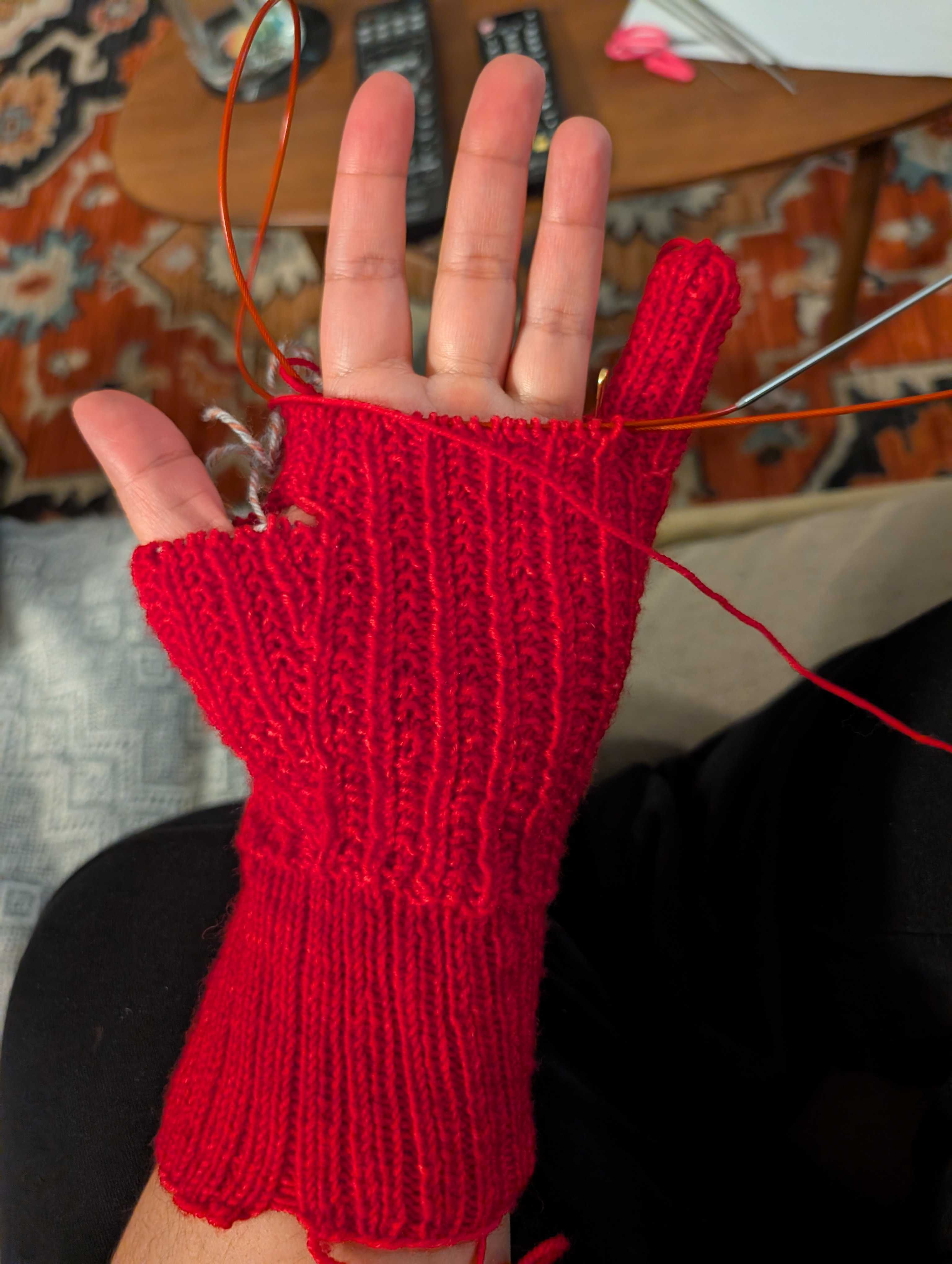 A half-finished red knit glove, with half a thumb, most of a hand, and one finished pinky finger