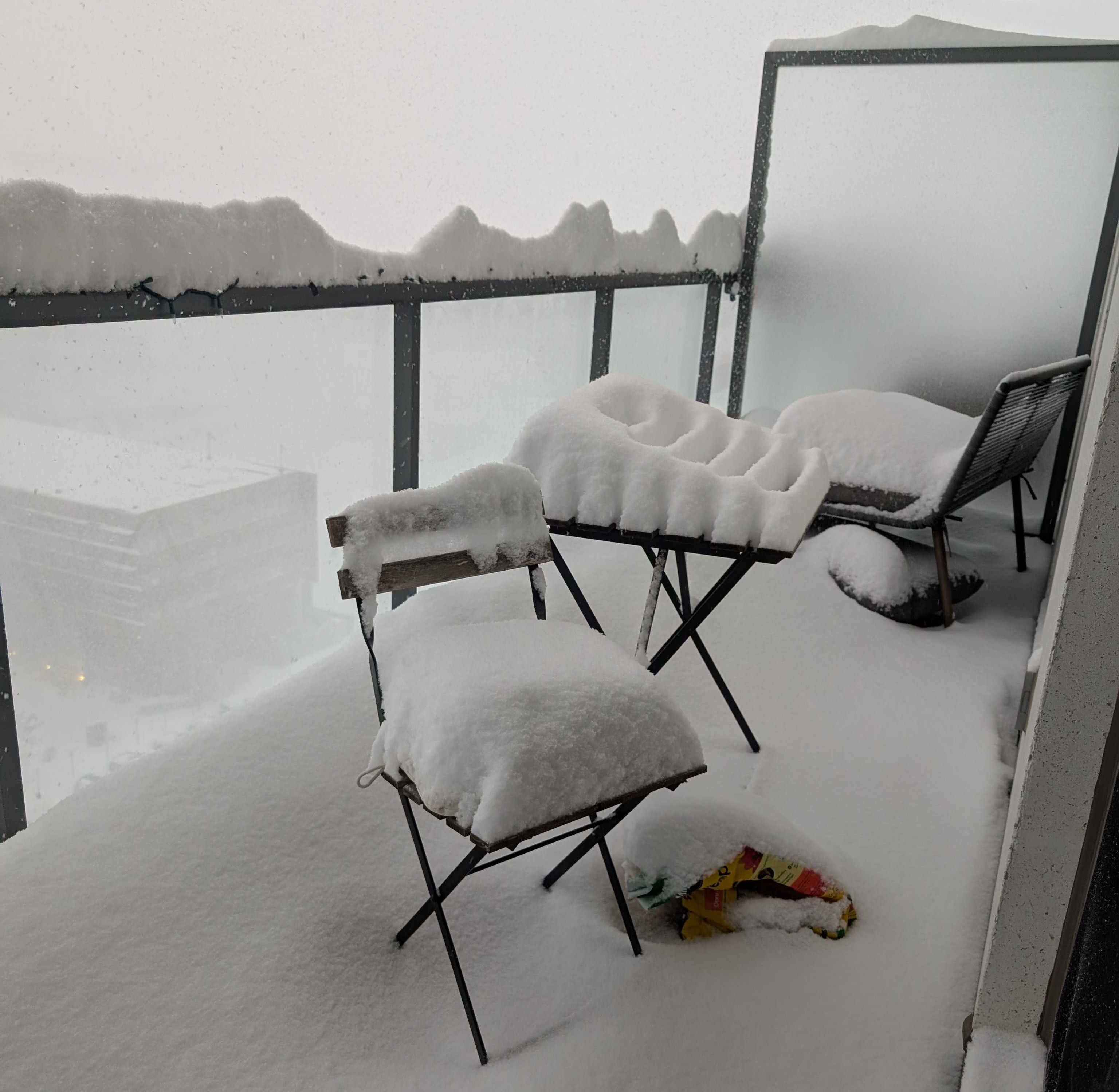 A fairly preposterous amount of snow piled on a balcony, with a snowstorm still happening